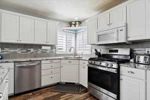Kitchen with stainless steel appliances, a sink, white cabinets, and dark wood finished floors