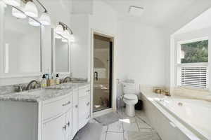 Full bath with a bath, toilet, double vanity, marble look tile flooring, and a stall shower