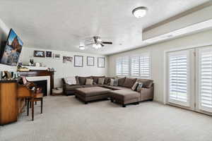 Living area with ceiling fan, light carpet, a warm lit fireplace, and a textured ceiling