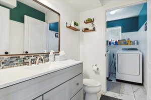 Bathroom with independent washer and dryer, toilet, vanity, marble look tiles, and backsplash
