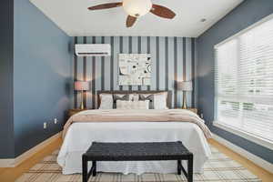 Bedroom with a wall mounted air conditioner, wood finished floors, baseboards, and a ceiling fan