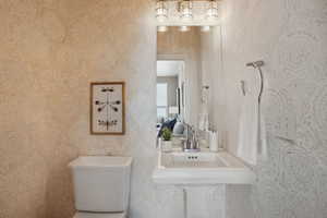 Half bathroom with toilet, a sink, and wallpapered walls