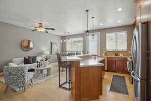 Kitchen featuring stainless steel appliances, light countertops, open floor plan, light wood finished floors, and brown cabinets