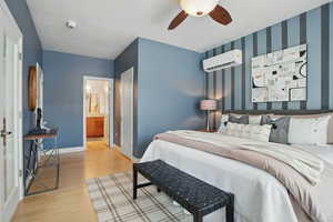Bedroom with a wall unit AC, wood finished floors, wallpapered walls, baseboards, and ensuite bath