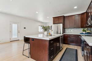 Kitchen featuring appliances with stainless steel finishes, light wood finished floors, a center island with sink, decorative backsplash, and light countertops