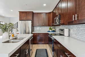 Kitchen with appliances with stainless steel finishes, a sink, light countertops, light wood-style flooring, and recessed lighting