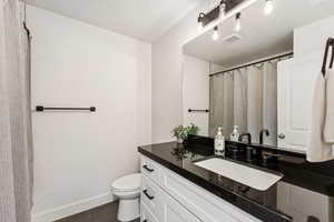 Full bath with toilet, vanity, baseboards, and a shower with shower curtain
