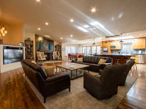 Large Great room featuring recessed lighting, a large fireplace, wood finished floors, vaulted ceiling