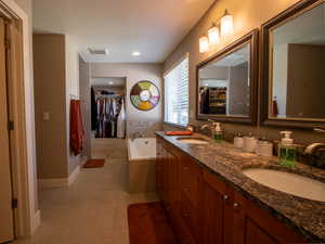 Full bathroom featuring double vanity, a garden tub, baseboards, a textured ceiling, and a spacious closet
