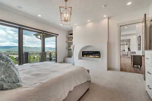 Carpeted bedroom with access to exterior, recessed lighting, a glass covered fireplace, a mountain view, and a chandelier