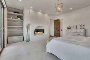 Carpeted bedroom with recessed lighting, a glass covered fireplace, and a chandelier