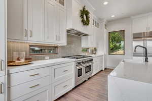 Kitchen featuring premium appliances, a sink, custom range hood, light wood-style floors, and recessed lighting