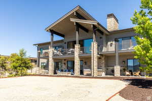 View of front of house featuring a balcony, stone siding, a chimney, and a patio