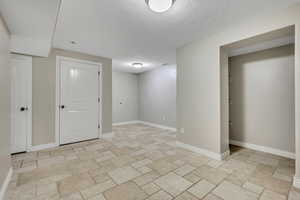 Unfurnished room featuring a textured ceiling, baseboards, and light stone finish floors