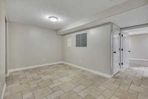 Finished basement with electric panel, a textured ceiling, and baseboards