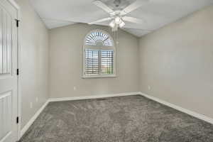 Spare room featuring carpet floors, ceiling fan, baseboards, and lofted ceiling
