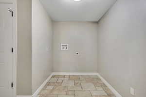 Washroom with hookup for an electric dryer, hookup for a washing machine, stone tile flooring, baseboards, and a textured ceiling