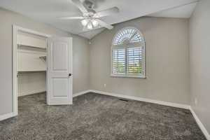 Unfurnished bedroom with carpet, vaulted ceiling, a walk in closet, baseboards, and a ceiling fan