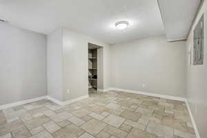 Spare room with a textured ceiling, light stone finish floors, and baseboards