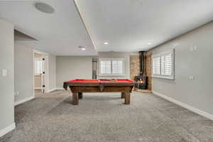 Playroom with a wood stove, a textured ceiling, baseboards, carpet flooring, and billiards
