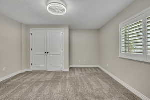 Unfurnished bedroom with carpet flooring, a textured ceiling, baseboards, and a closet