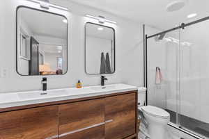 Bathroom featuring double vanity, a stall shower, and toilet