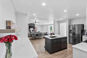 Kitchen featuring stainless steel fridge, a sink, dishwasher, a center island with sink, and a ceiling fan