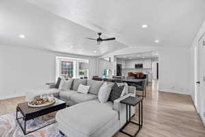 Living area with a ceiling fan, light wood-style floors, vaulted ceiling, baseboards, and recessed lighting