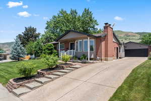 View of front facade featuring a chimney, covered porch, a front yard, brick siding, and a mountain view