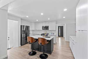 Kitchen with stainless steel appliances, light countertops, a kitchen island with sink, decorative backsplash, and light wood finished floors