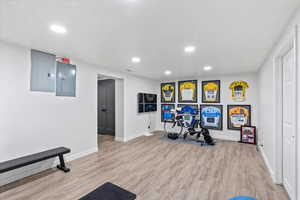 Exercise area with electric panel, recessed lighting, light wood-style floors, and baseboards