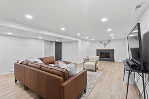 Living room with a brick fireplace, light wood finished floors, baseboards, and recessed lighting