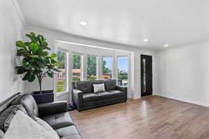 Living room with ornamental molding, plenty of natural light, wood finished floors, recessed lighting, and baseboards