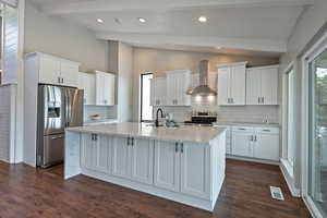 Kitchen featuring wall chimney exhaust hood, stainless steel appliances, a sink, an island with sink, and white cabinetry