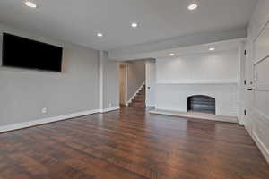 Unfurnished living room with baseboards, a fireplace, recessed lighting, wood finished floors, and stairs