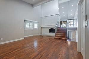 Unfurnished living room with a towering ceiling, stairway, wood finished floors, baseboards, and a fireplace