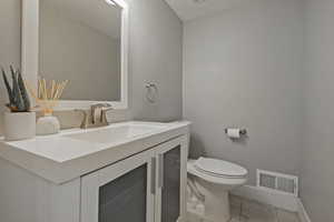 Half bathroom with toilet, vanity, baseboards, and tile patterned flooring