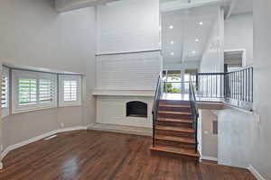 Unfurnished living room with wood finished floors, stairs, a high ceiling, a fireplace, and baseboards