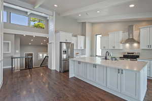 Kitchen with wall chimney range hood, appliances with stainless steel finishes, high vaulted ceiling, a sink, and a center island with sink