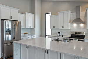 Kitchen with stainless steel appliances, wall chimney exhaust hood, white cabinets, backsplash, and lofted ceiling
