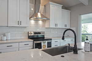 Kitchen featuring wall chimney range hood, stainless steel electric range, white cabinetry, tasteful backsplash, and vaulted ceiling