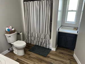 Full bath with wood finished floors, toilet, vanity, and baseboards