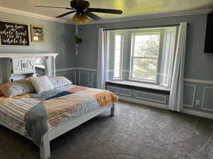 Carpeted bedroom featuring crown molding, a wainscoted wall, and a ceiling fan
