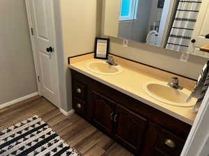 Full bath with wood finished floors, double vanity, and baseboards