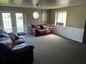 Living room with carpet flooring, a textured ceiling, a wainscoted wall, and french doors