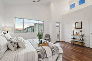 Bedroom with dark wood-style flooring, multiple windows, a high ceiling, and baseboards
