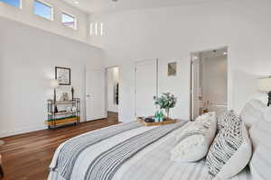 Bedroom featuring wood finished floors, baseboards, a towering ceiling, ensuite bath, and recessed lighting