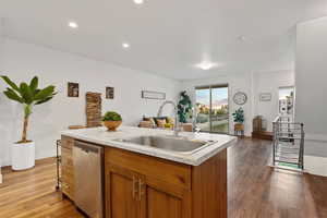 Kitchen with stainless steel dishwasher, a sink, light countertops, open floor plan, and wood finished floors