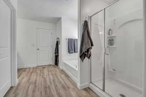 Full bathroom featuring wood finished floors, a stall shower, a garden tub, and baseboards