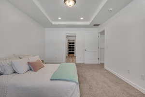 Carpeted bedroom with a tray ceiling, baseboards, a walk in closet, and recessed lighting